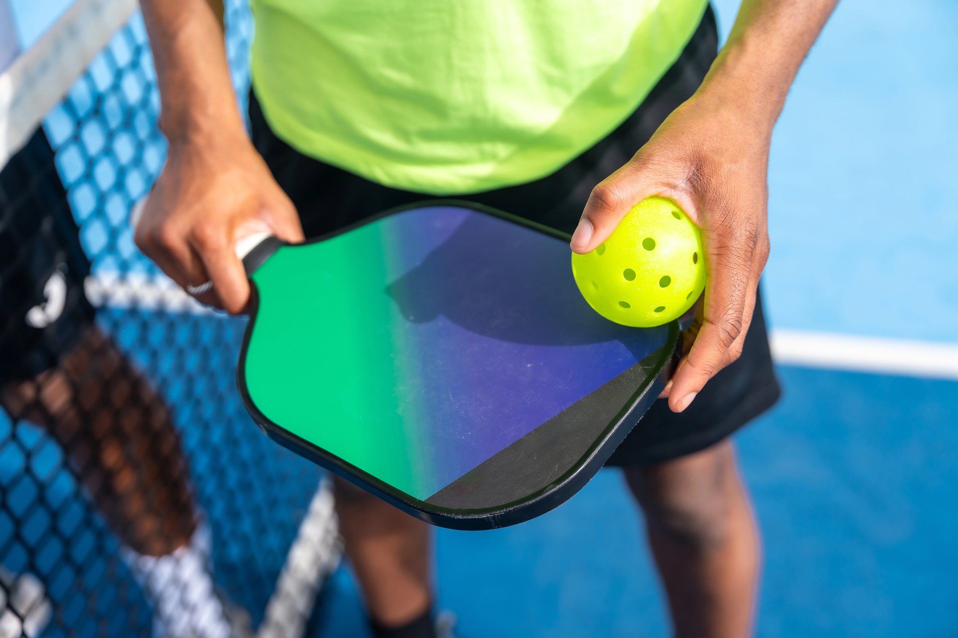 Jugador sujetando una pala y una bola de pickleball junto a la red